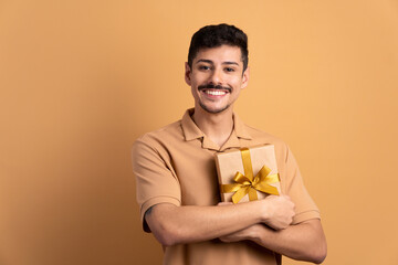 joyful brazilian man with gift box present in beige colors. christmas, happy birthday, celebration...