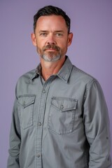 Obraz premium Confident Middle-Aged Man in Grey Shirt Against Soft Lavender Background for Professional Use