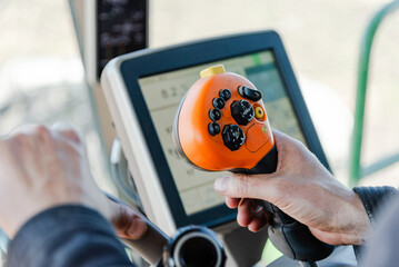 Farmer Operating Auger Joystick in Combine Harvesting Soybeans, Steering Wheel and Tractor Computer Visible in Field, Close-Up of Hand Controlling Farm Equipment During Busy Harvest Season