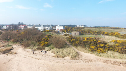 Aerial view of coastal landscape. Sandy beach, colourful houses in distance and golf course visible on the hillside