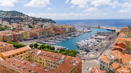 Aerial view of Nice, France, showcasing the vibrant Port of Nice, with colorful buildings, yachts, and a scenic Mediterranean backdrop. The city blends historic charm with coastal beauty