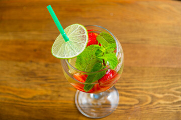 Glass with non-alcoholic cocktail strawberry mint lime with ice on wooden table