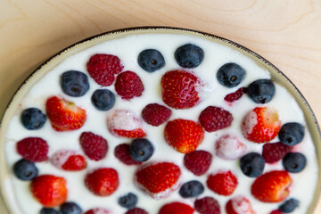 In a plate with whipped cream, ripe berries strawberries, raspberries and blueberries on a light background