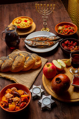 Challah, honey, apple and pomegranate and wine and chelnt and fish on the table