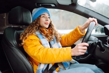 Happy woman in winter outfit driving car. The concept of transport, lifestyle.