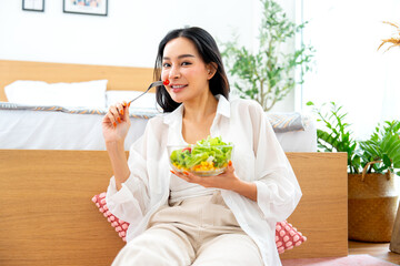 Pretty Asian woman hold bowl of vegetable salad and she express happy with eating and look at camera with smiling.