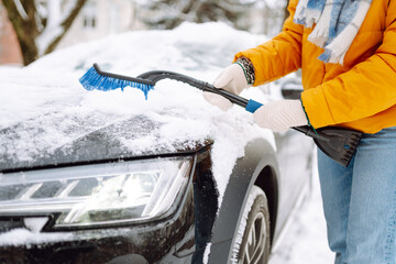 Portrait of smiling woman cleaning snow off his car during winter snowfall. Scraping ice.