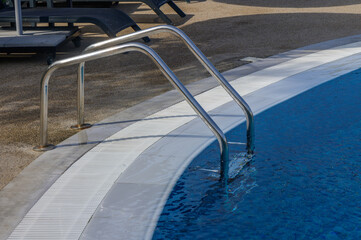 Stainless steel ladder leading into a clear swimming pool at a sunny outdoor leisure area