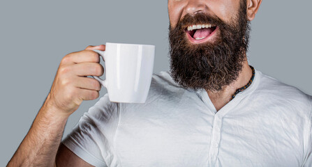 Close up portrait of a bearded man holding a mug and smiling. Happy man holding tea mug. Hipster with beard holds mug. Man with happy face try to awake with cup of coffee