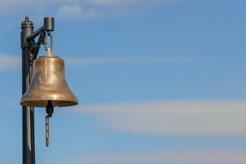 shiny station bell with chain against blue sky with clouds