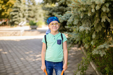 A playful small boy in glasses and a headband, dressed in a green shirt and jean shorts, laughing