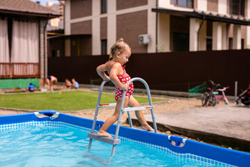 Happy little girl in red swimsuit jumping into outdoor swimming pool at home. Baby girl learning to swim. Water fun for children.