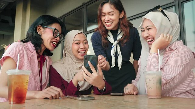 Asian girl friends from Indonesia sitting in cafe using mobile phone together to share content on social media