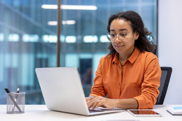 Young professional woman working on a laptop in modern office with tablet and smartphone on desk