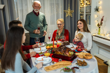 Grandfather is making a toast at the table. Family celebrating Christmas together eating homemade food.
