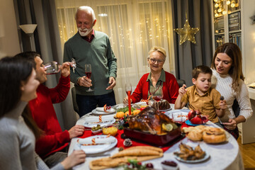Grandfather is making a toast at the table. Family celebrating Christmas together eating homemade food.