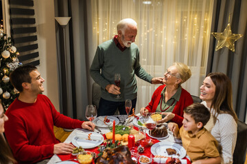 Grandfather is making a toast at the table. Family celebrating Christmas together eating homemade food.
