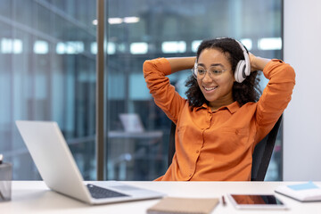 Relaxed woman enjoying music with headphones in modern office environment while taking a break from work and feeling happy and comfortable