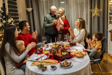 Grandparents giving presents to eachother on Christmas Eve. Family having dinner.