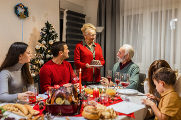 Grandmother brought tasty cake on the dining table. Family celebrating Christmas.