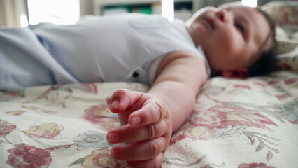 Baby lying comfortably on a patterned blanket, reaching out with one arm. The scene captures the baby’s full body while relaxing in a cozy home setting