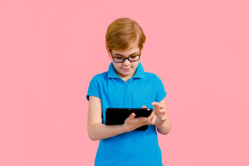 Boy wearing glasses using a tablet on a pink background