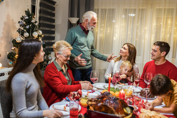 Grandfather is making a toast at the table. Family celebrating Christmas together eating homemade food.