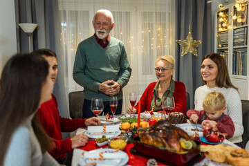 Grandfather is making a toast at the table. Family celebrating Christmas together eating homemade food.