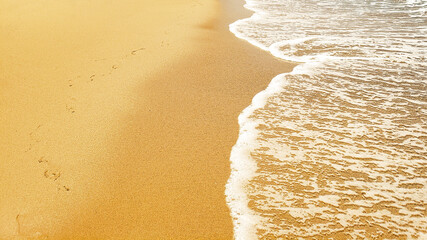 Fototapeta na wymiar Full frame of beach coastline meeting ocean with light footprints in the sand background texture