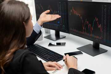 Two business traders discussing on dynamic stock market in currency rate investment trading on two pc screens with compare real time graph on risk or profit point of data at modern office. Postulate.