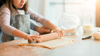 Father and daughter rolling dough together in kitchen to make cookies, using wooden rolling pin, cooking at home, enjoying homemade pastry, preparing pizza, love baking, cropped image with free space