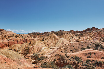 Striking landscape features expansive hills with vibrant hues of red, orange, tan, characteristic of desert environment. terrain is rugged and undulating, natural scene, Fairy Tale canyon, Kyrgyzstan