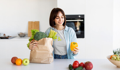 Young lady unpacking grocery bag after shopping, putting vegetables on table in kitchen interior at home, copy spsce. Dinner preparation and household leisure concept