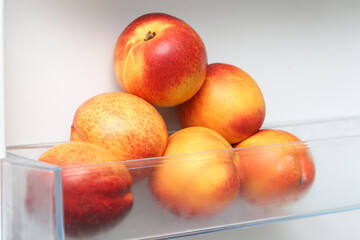 Nectarines in fridge. Isolated on white fridge door. Fresh yellow and red nectarines. Ripe bunch of nectarines on a transparent refrigerator shelf and in a plastic fridge drawer. Pile of fruits.
