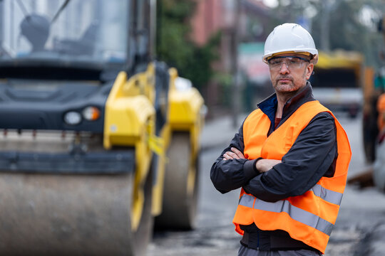 Construction worker in safety gear oversees machinery operation on a busy urban site during daylight hours