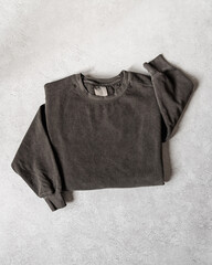 Blank Dark Gray Crewneck Sweatshirt Folded on Concrete Background, Stylized Sleeves, Natural Lighting with Bold Shadows, Simple Product Shot with Blank Tag, Casual Apparel Photography Mockup Template