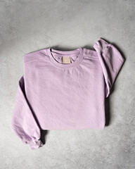 Blank Purple Lilac Crewneck Sweatshirt Folded Concrete Background, Stylized Sleeves, Natural Lighting with Bold Shadows, Simple Product Shot with Blank Tag, Casual Apparel Photography Mockup Template