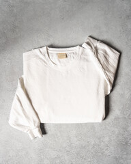 Blank White Cream Crewneck Sweatshirt Folded Concrete Background, Stylized Sleeves, Natural Lighting with Bold Shadows, Simple Product Shot with Blank Tag, Casual Apparel Photography Mockup Template