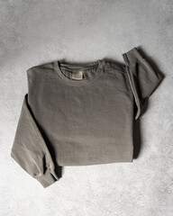 Blank Grey Crewneck Sweatshirt Folded on Concrete Background, Stylized Sleeves, Natural Lighting with Bold Shadows, Simple Product Shot with Blank Tag, Casual Apparel Photography Mockup Template