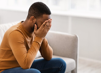 Male Depression. Desperate Depressed African Man Covering Face Crying Having Problems Sitting On Couch At Home. Emotional Stress And Unhappiness Concept. Despair, Grief And Negative Emotions