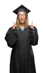 Young beautiful woman wearing graduated uniform over isolated background amazed and surprised looking up and pointing with fingers and raised arms.