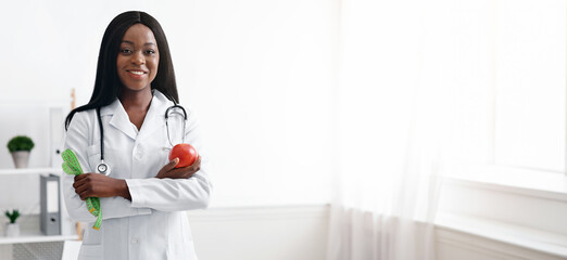 Friendly black woman dietician with apple and tape recommending fruits and vegetables during...