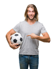 Young handsome man with long hair over isolated background holding football ball very happy pointing with hand and finger