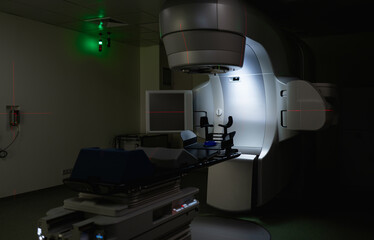 Dimly lit treatment room with linear accelerator ready for radiotherapy. Red laser lines highlight...
