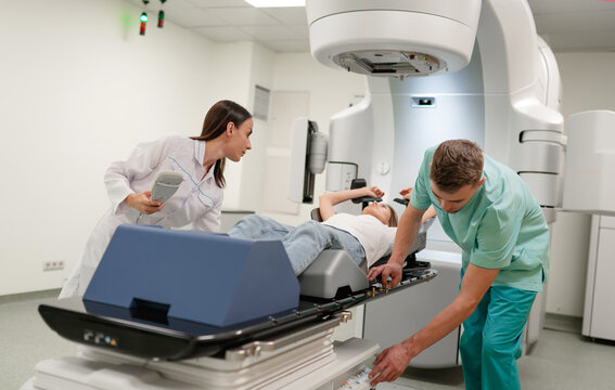 Two healthcare professionals prepare patient for radiotherapy treatment using linear accelerator. The advanced machine and precise setup highlight modern medical environment focused on patient care