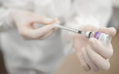 A close-up of a healthcare worker's hands wearing gloves, preparing a syringe with a vaccine or medication from a vial, highlighting vaccination, medical treatment, and safety protocols.