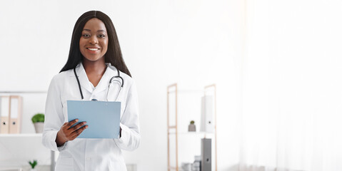 Positive afro woman professional dietologist holding medical chart in her office, smiling at...