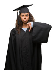 Young hispanic woman wearing graduation uniform with angry face, negative sign showing dislike with thumbs down, rejection concept