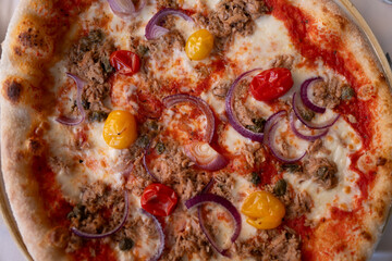Close-up of pizza topped with tuna, red onion, and heritage tomatoes
