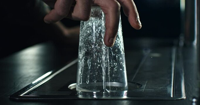 Super slow motion close up of barman or bartender washing transparent glass with automatic glass rinser with water spray and splashing drops in bar at 1000 fps.